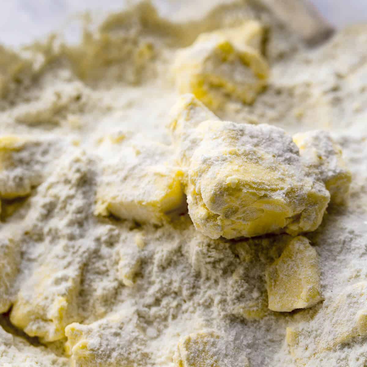 Cold, cubed unsalted butter sitting on top of all-purpose flour and salt in a mixing bowl for savory cookies.