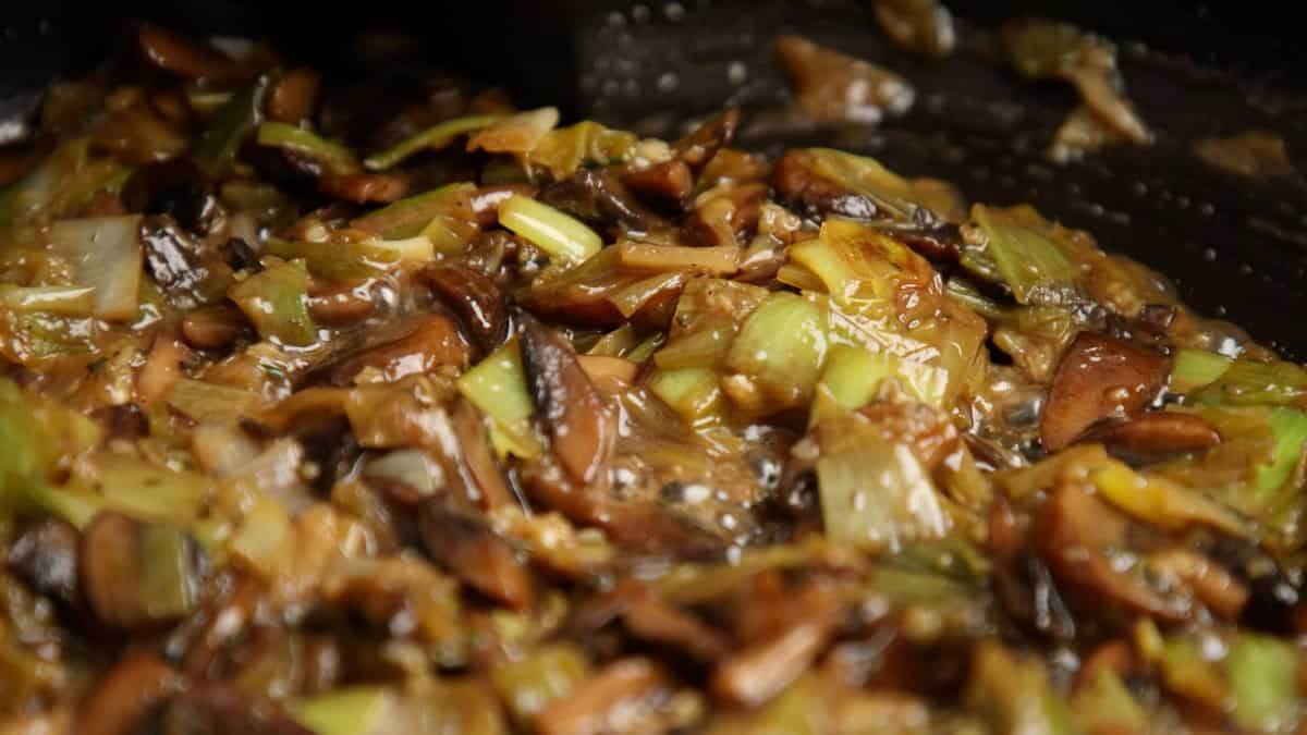 Cooked, deeply browned mushroom and leek base in a black pan.