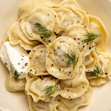 Russian pelmeni with sour cream and dill in a white ceramic bowl.