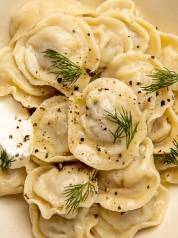 Russian pelmeni with sour cream and dill in a white ceramic bowl.