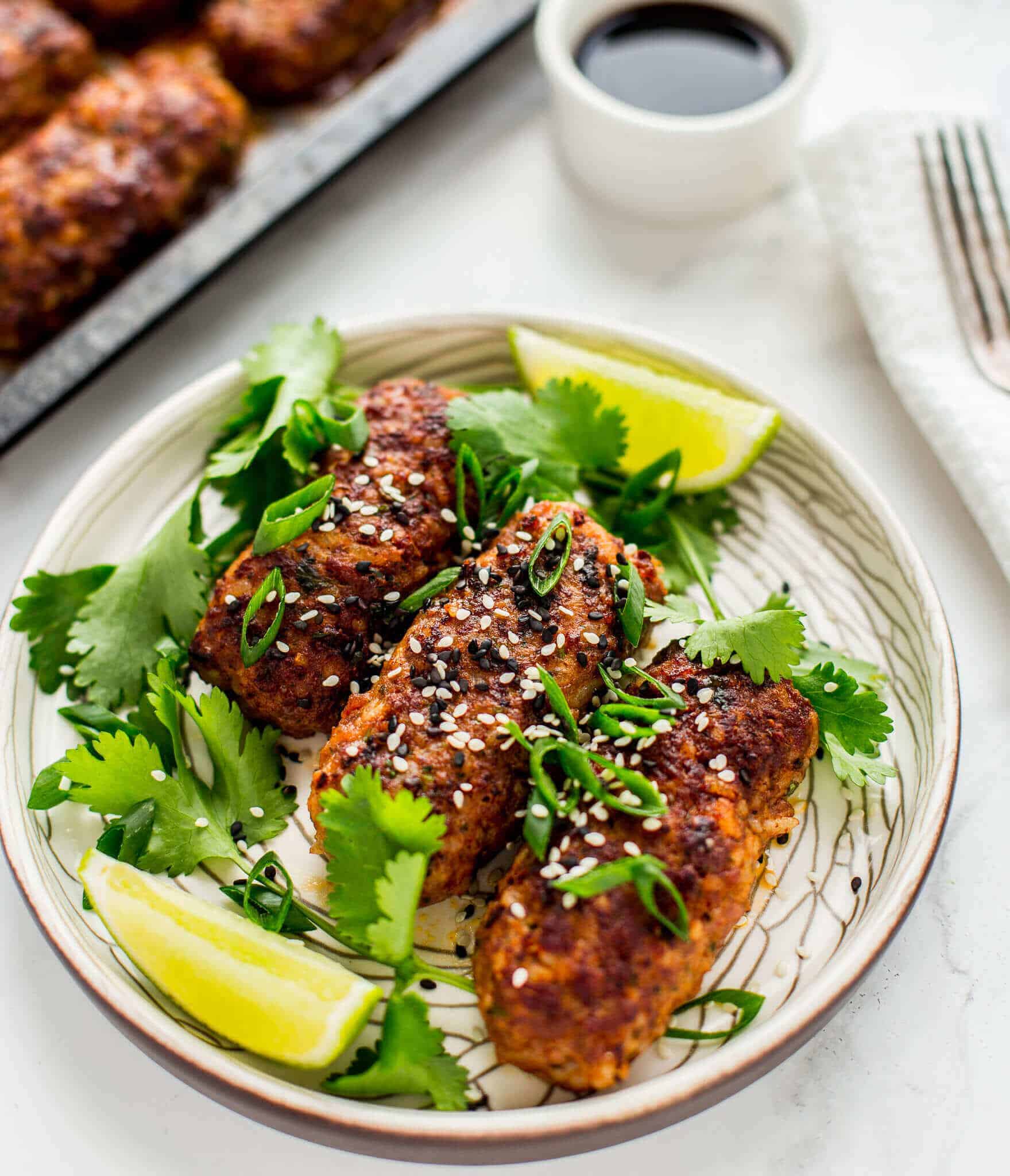 Thai spiced beef koftas with sesame, spring onion, soy and lime on a white plate.