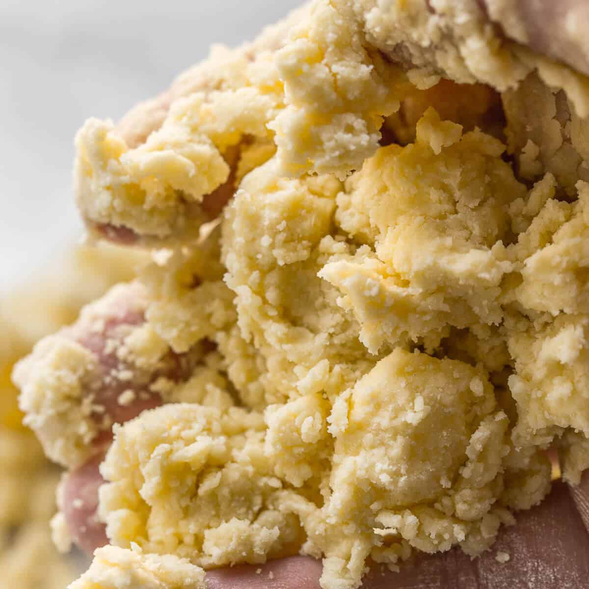Hands using the "sablé" technique to quickly rub cold butter into flour and salt for parmesan shortbread cookies.