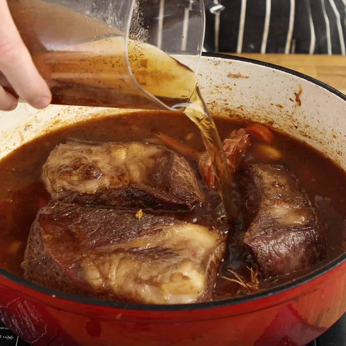 Adding seared beef and beef stock back into casserole for braising.