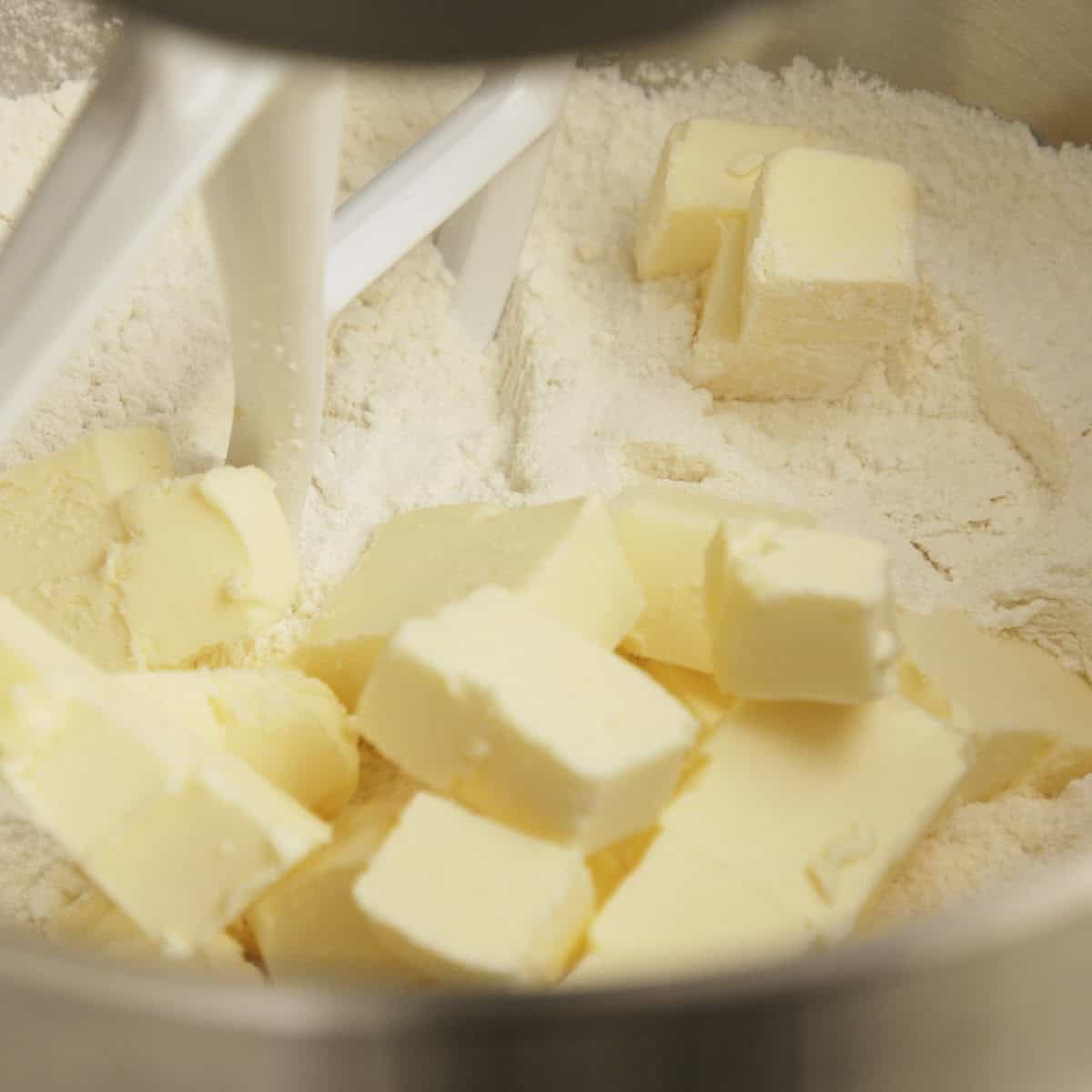 Butter cubes and flour in a metal bowl with a white paddle attachment.