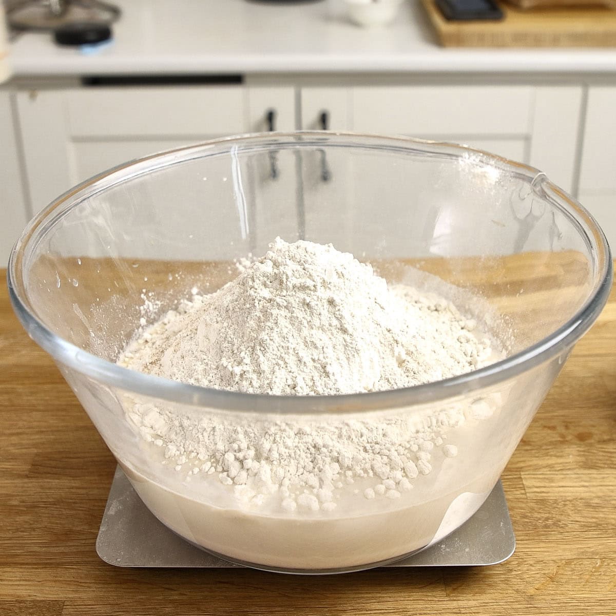 A clear bowl filled with white flour sits on a digital scale.