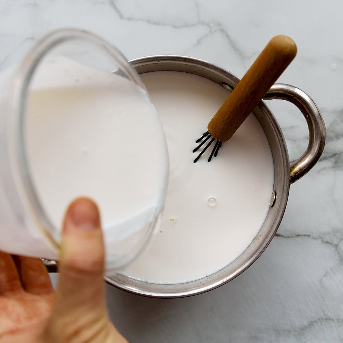 Adding kefir to milk in a pot.