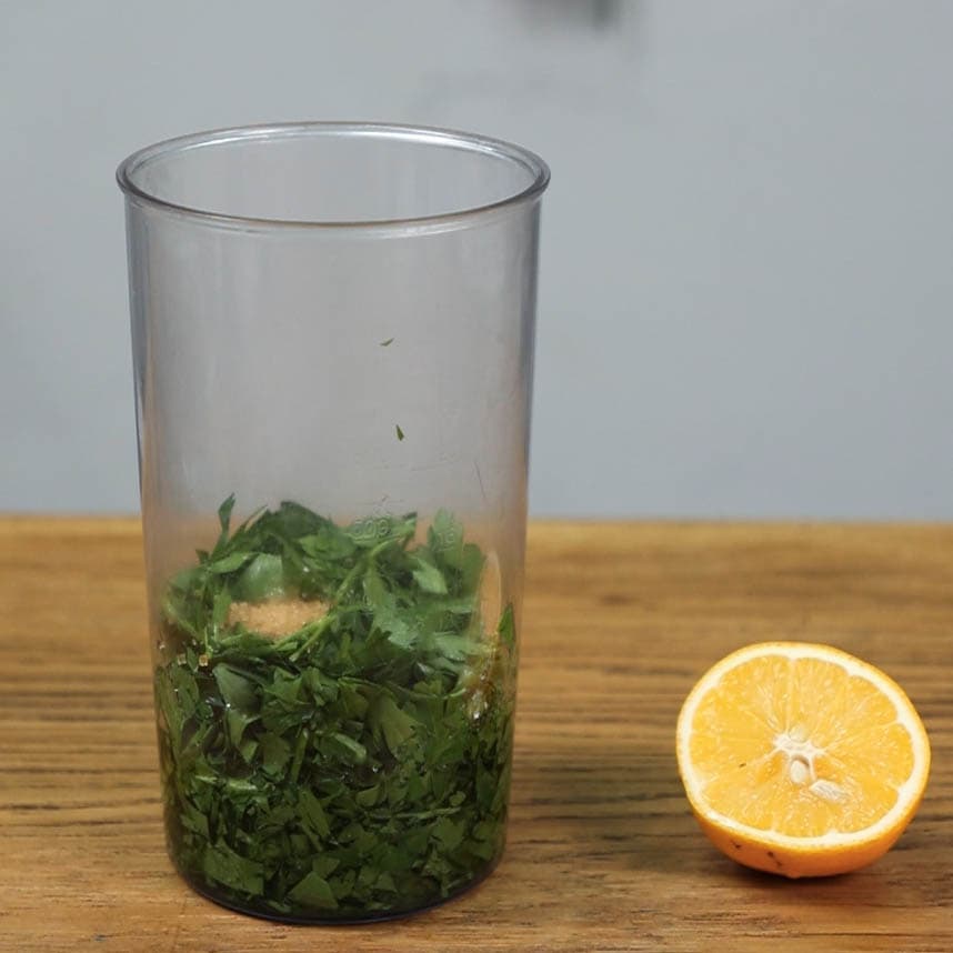 Herbs in a plastic jug next to half a lemon ready to add to sauce.