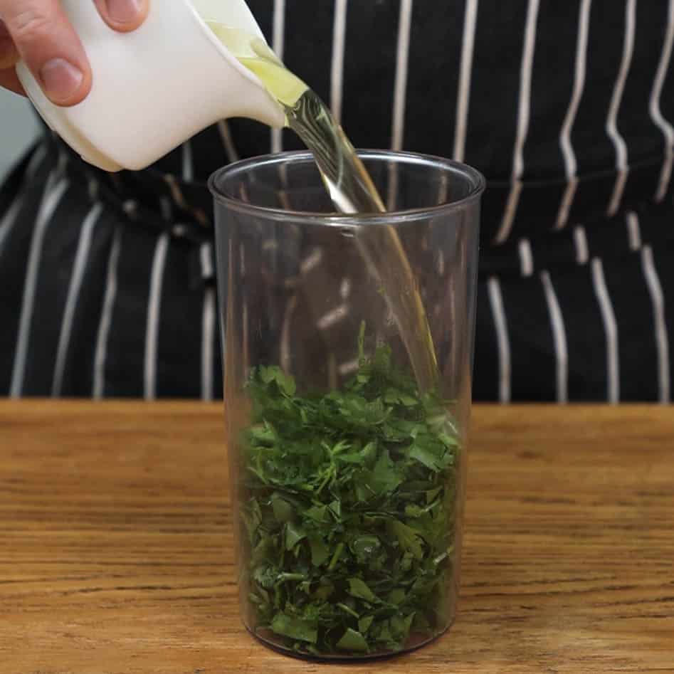 Adding oil to blender jug with herbs.