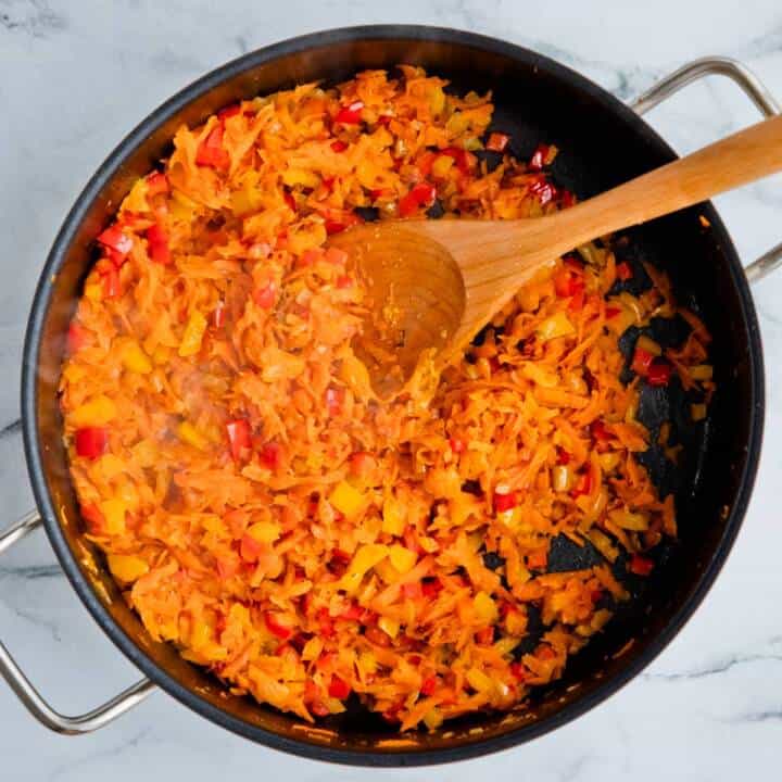Carrots, onions, and peppers cooking in a pan.