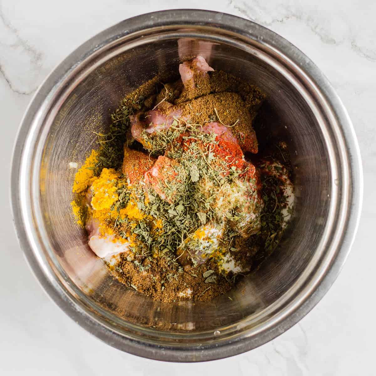 Adding spices to chicken in a metal bowl.