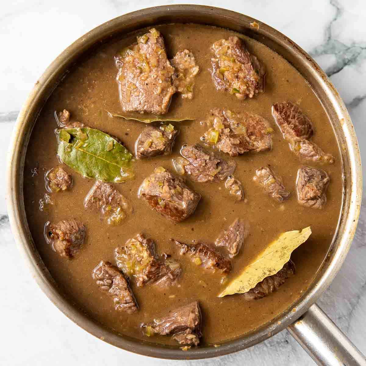 Meat with stock and spices in a pan.