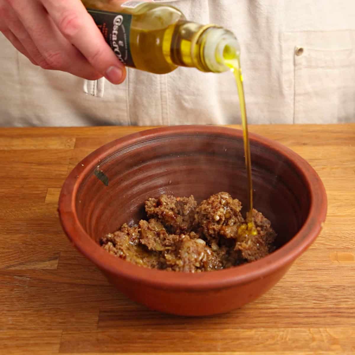 Adding truffle oil to cooked mushrooms in a brown bowl.