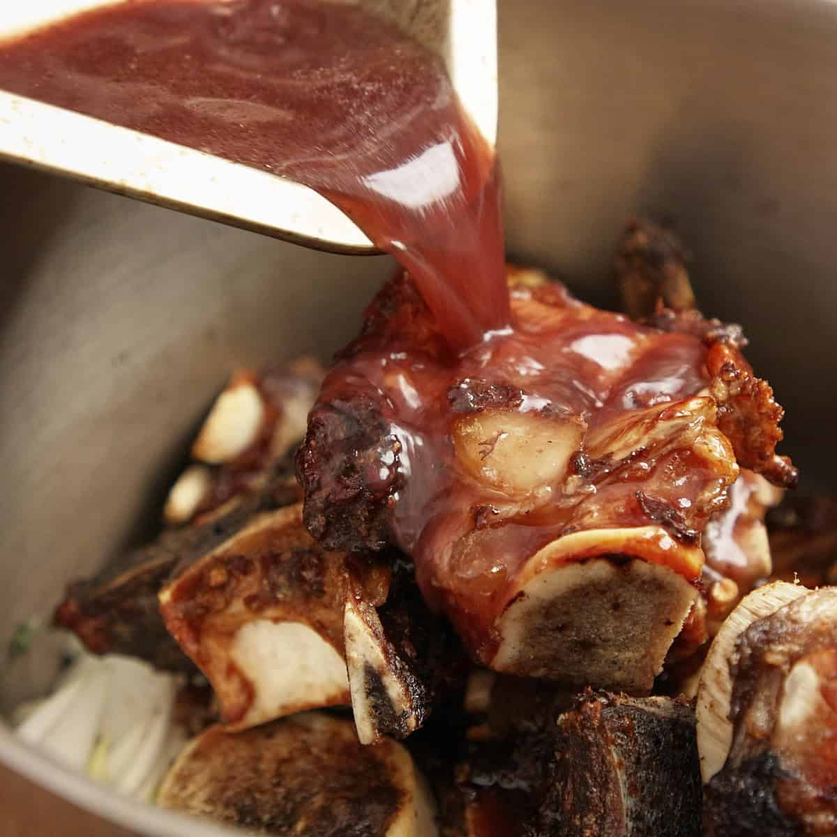 Adding deglazed wine to beef bones and mirepoix.