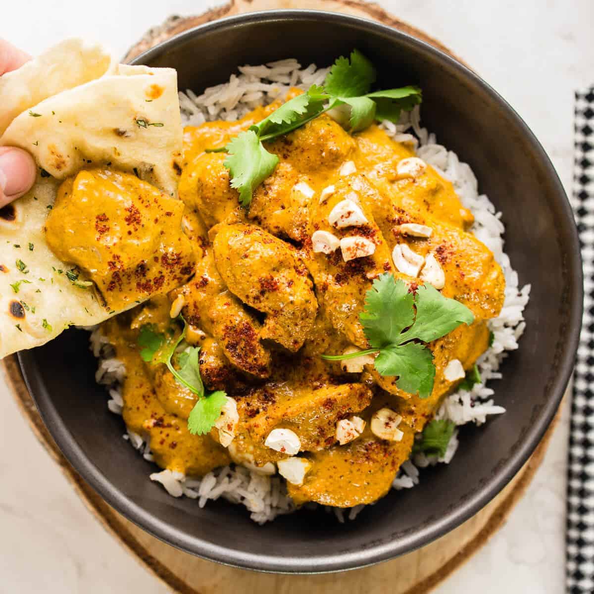 butter chicken on rice with flatbread in a black bowl