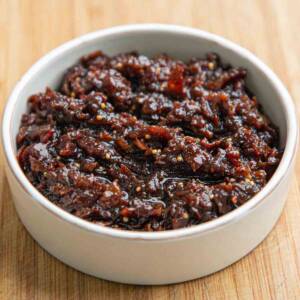 Bacon jam in a white ceramic dish on a wooden board.