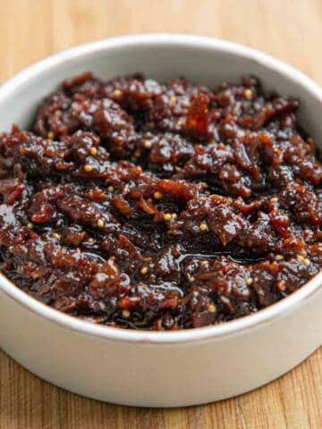 Bacon jam in a white ceramic dish on a wooden board.