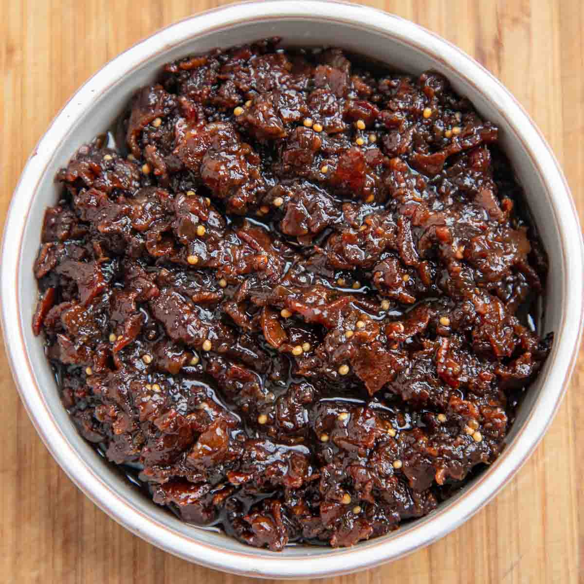 Bacon jam in a white ceramic dish on a wooden board.