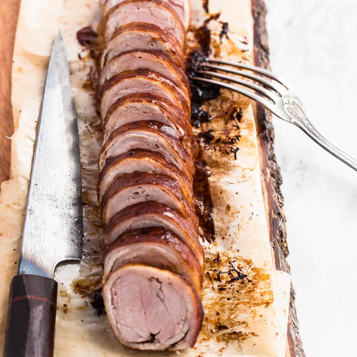 Cooked and sliced pork fillet wrapped in bacon on a wooden board