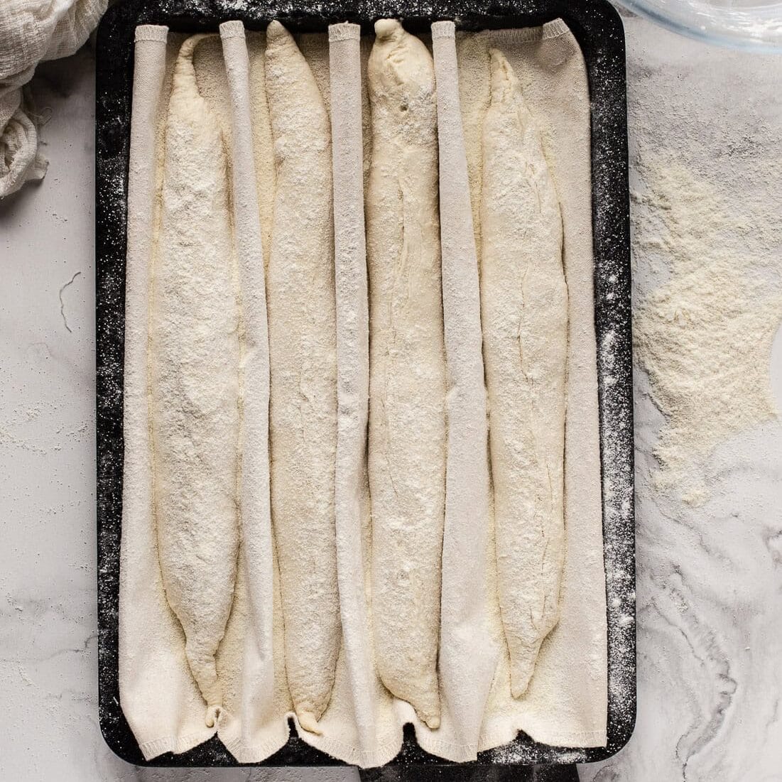 Placing baguettes onto a floured couche on a black tray.