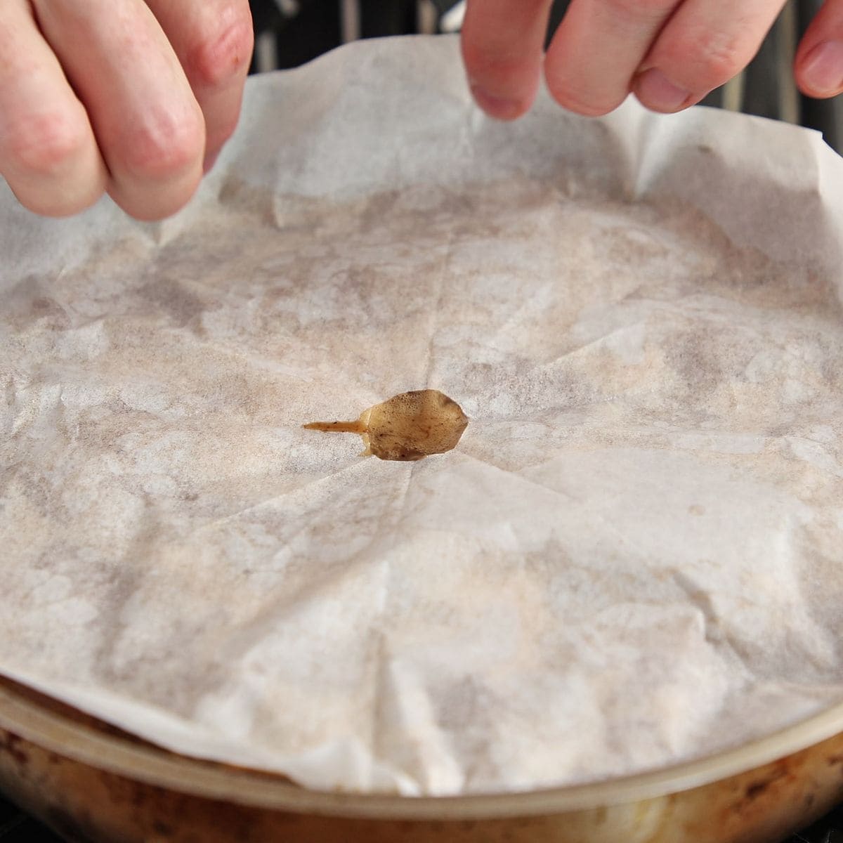 Pot covered with parchment paper cartouche cut to fit inside rim, liquid gently simmering underneath