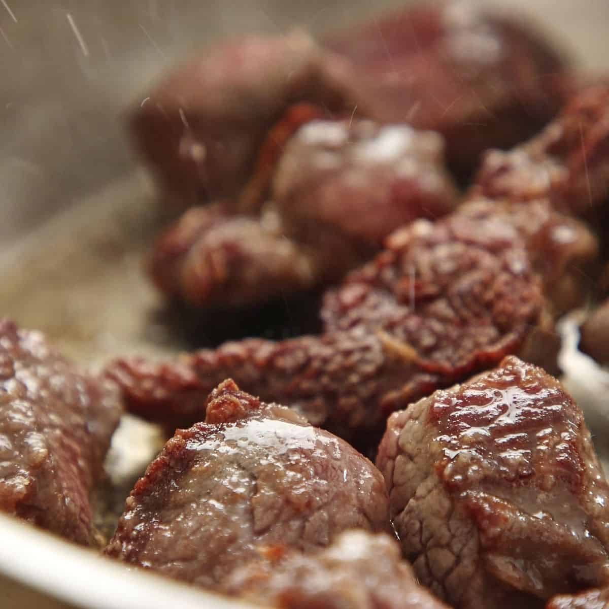 Beef chunks searing in heavy pot showing deep brown crust on all sides, single layer