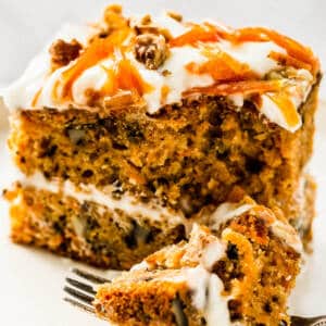 carrot cake with cream cheese frosting and carrot topping on white plate.