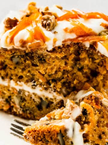 carrot cake with cream cheese frosting and carrot topping on white plate.