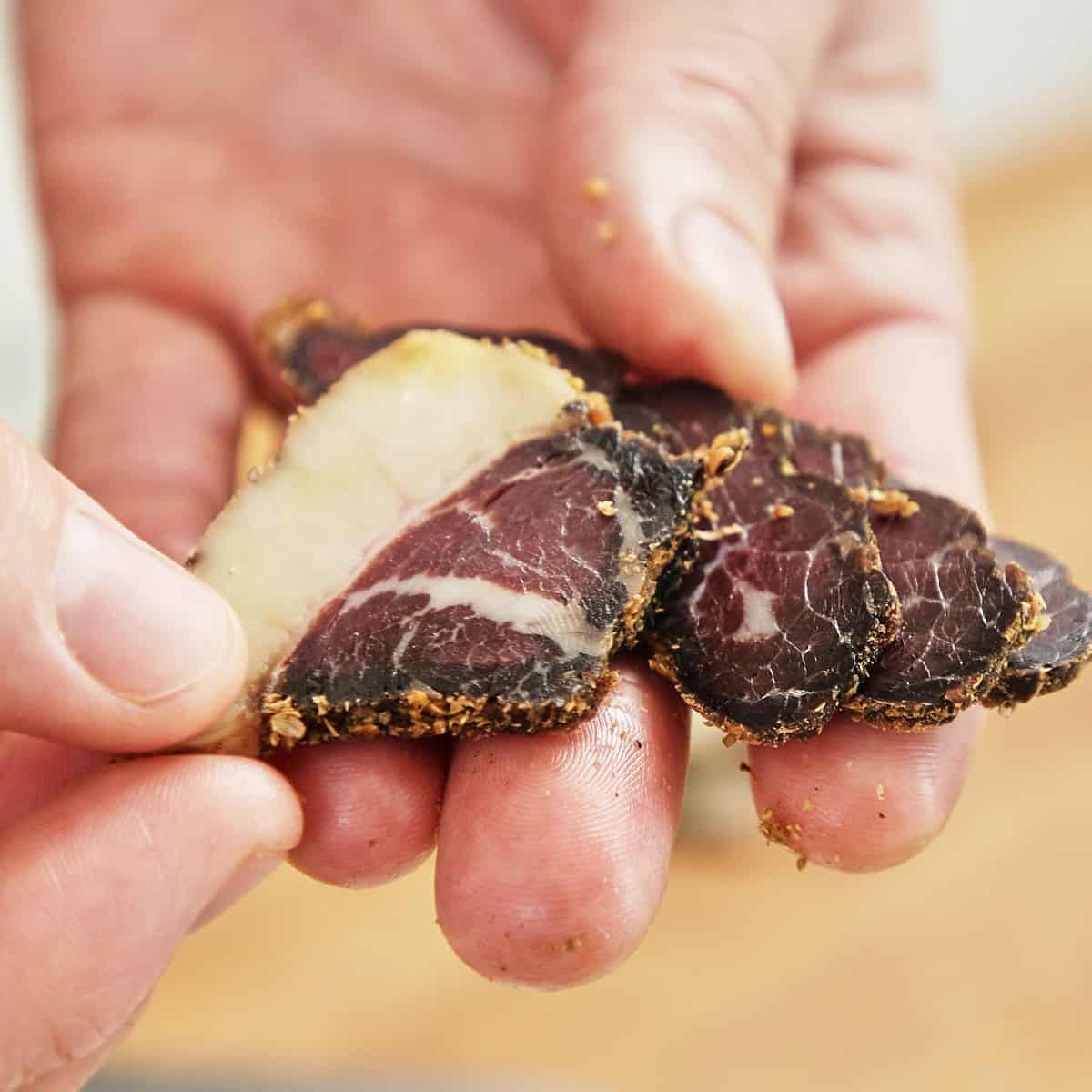 Sliced biltong with visible dark crust and pale interior held in hand.