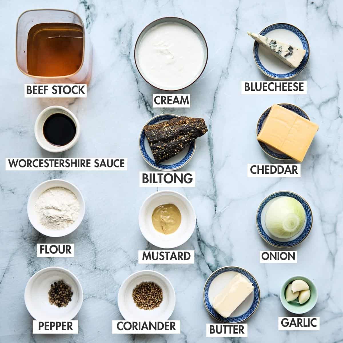 Mise en place for biltong soup arranged on marble: spices, flour, biltong strips, broth, butter, cream, mustard, onion, and cheese.