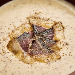 Seared biltong pieces nestled in creamy soup base with visible spice speckling.