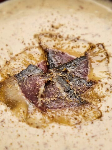 Seared biltong pieces nestled in creamy soup base with visible spice speckling.