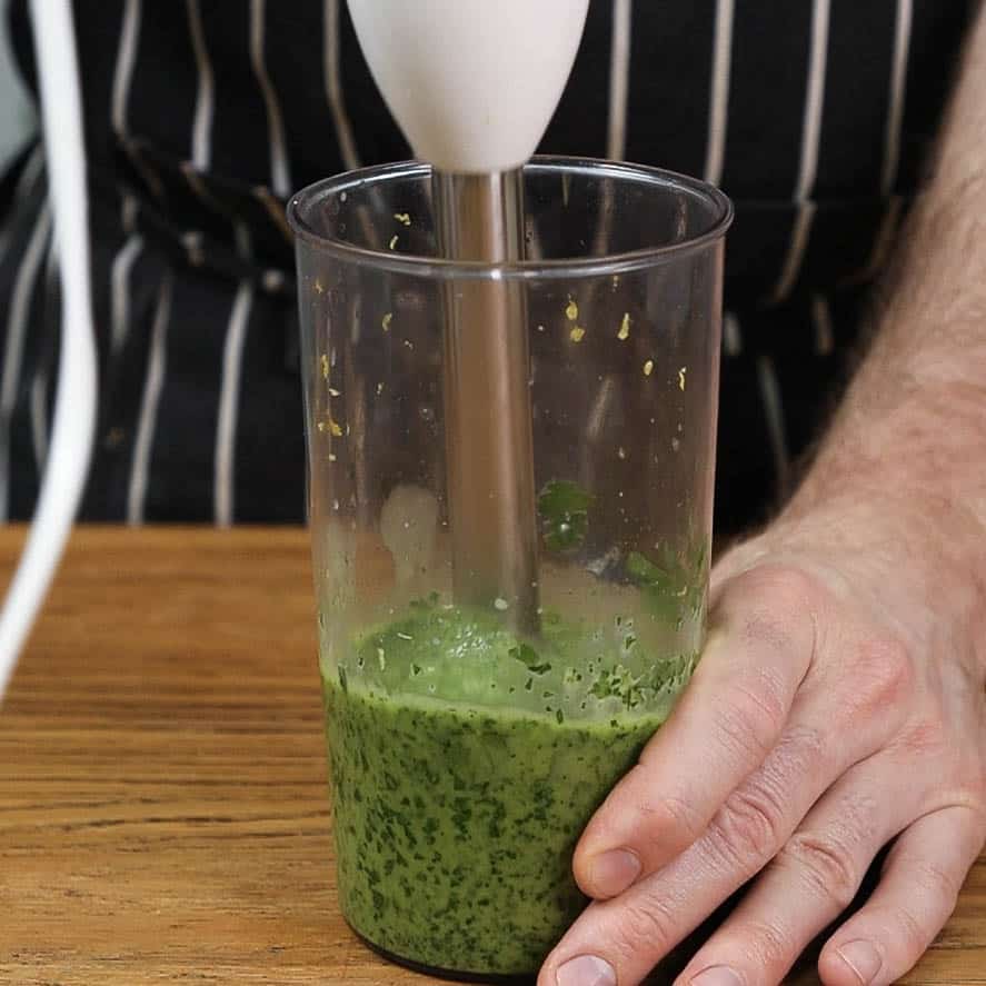 Blending gremolata in a jug with a blender.