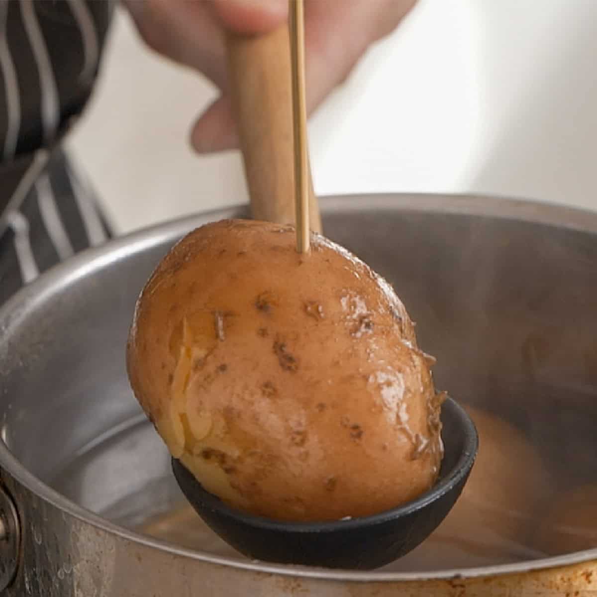 Testing boiled potatoes doneness with a wooden skewer.