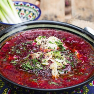 red ukrainian beet soup in black bowl on wooden table.