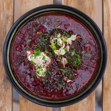 red ukrainian beet soup in black bowl on wooden table.