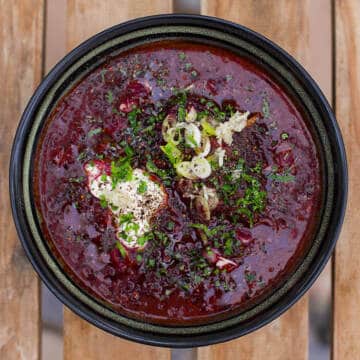 red ukrainian beet soup in black bowl on wooden table.