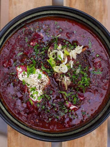 red ukrainian beet soup in black bowl on wooden table.