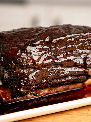 Braised beef short ribs with bbq glaze and red wine sauce on a white plate.