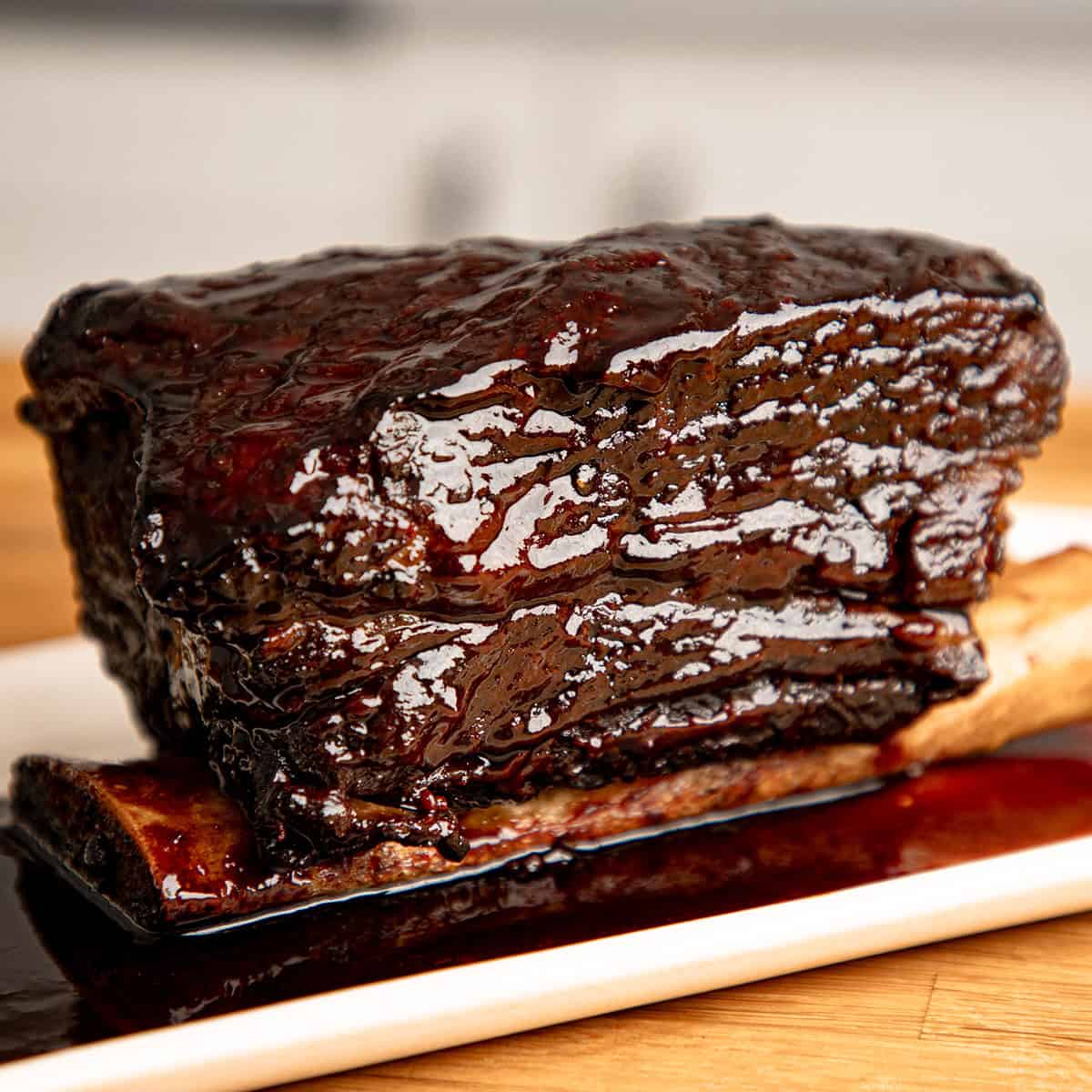 Braised beef short ribs with bbq glaze and red wine sauce on a white plate.