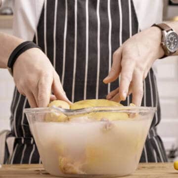 Brining chicken in salted water in a glass bowl.