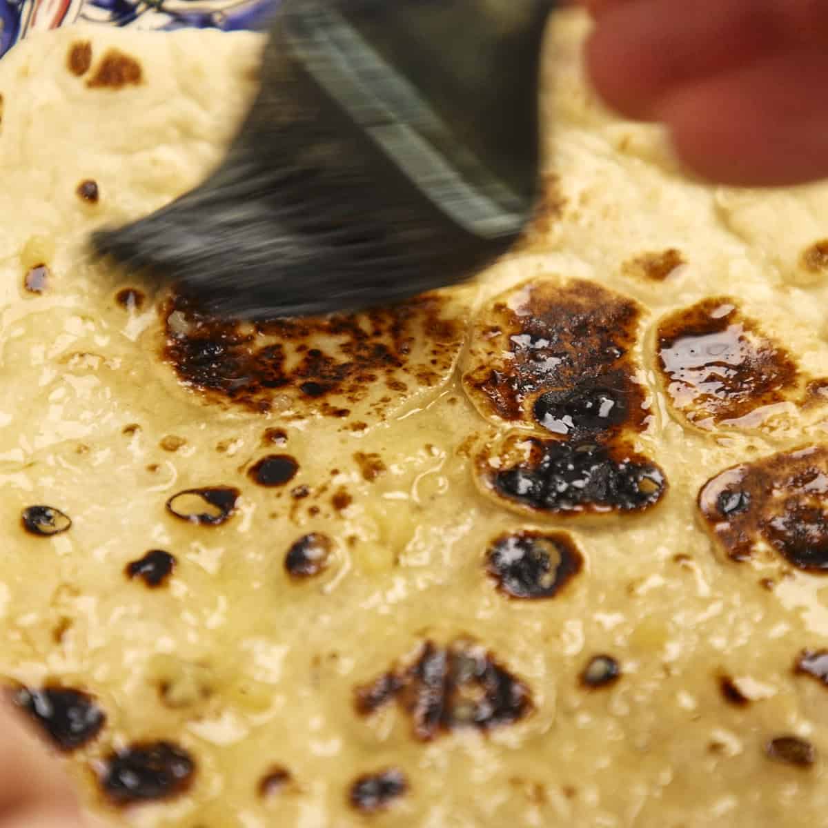 Brushing cooked naan with garlic butter.
