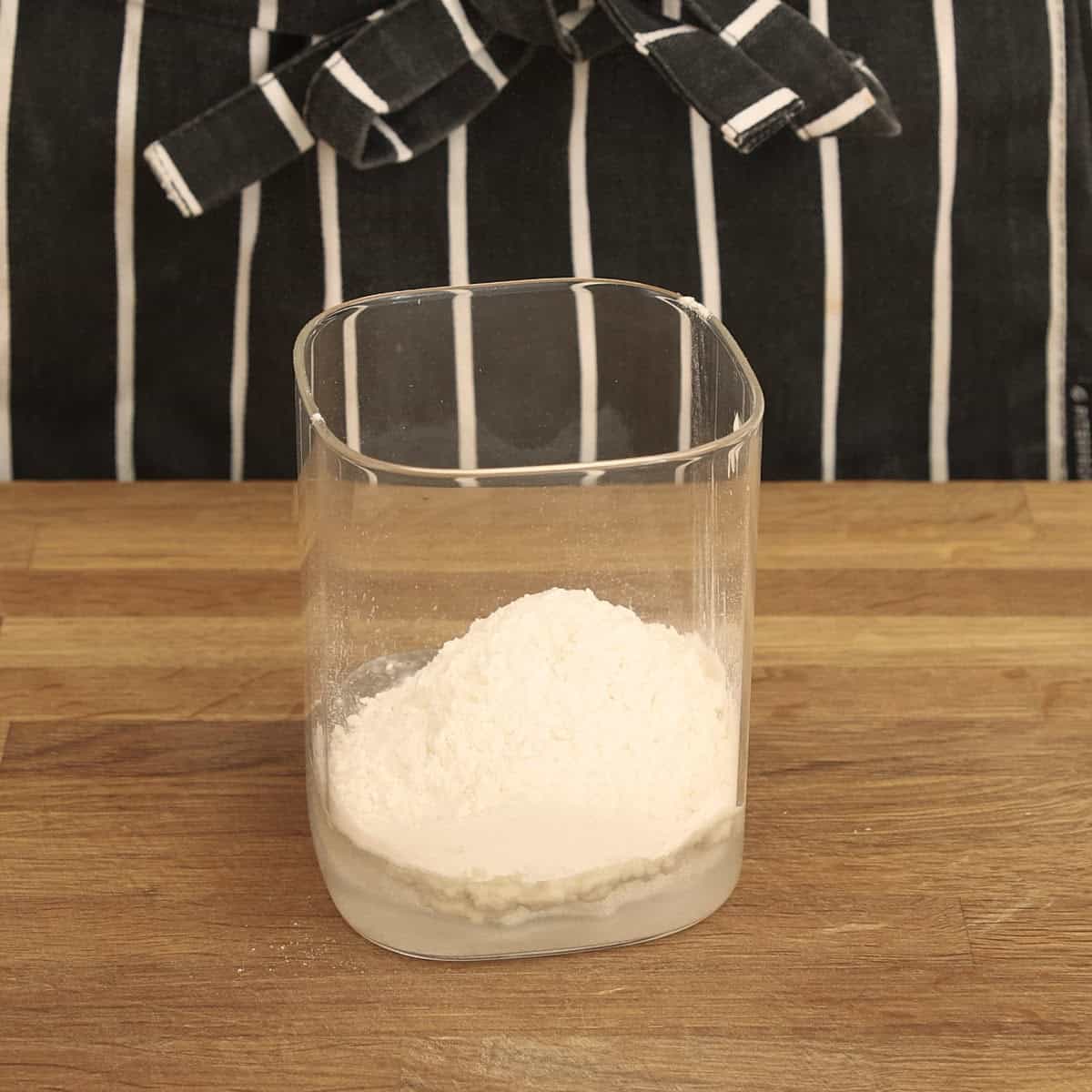 A clear glass jar contains flour, starter and water.