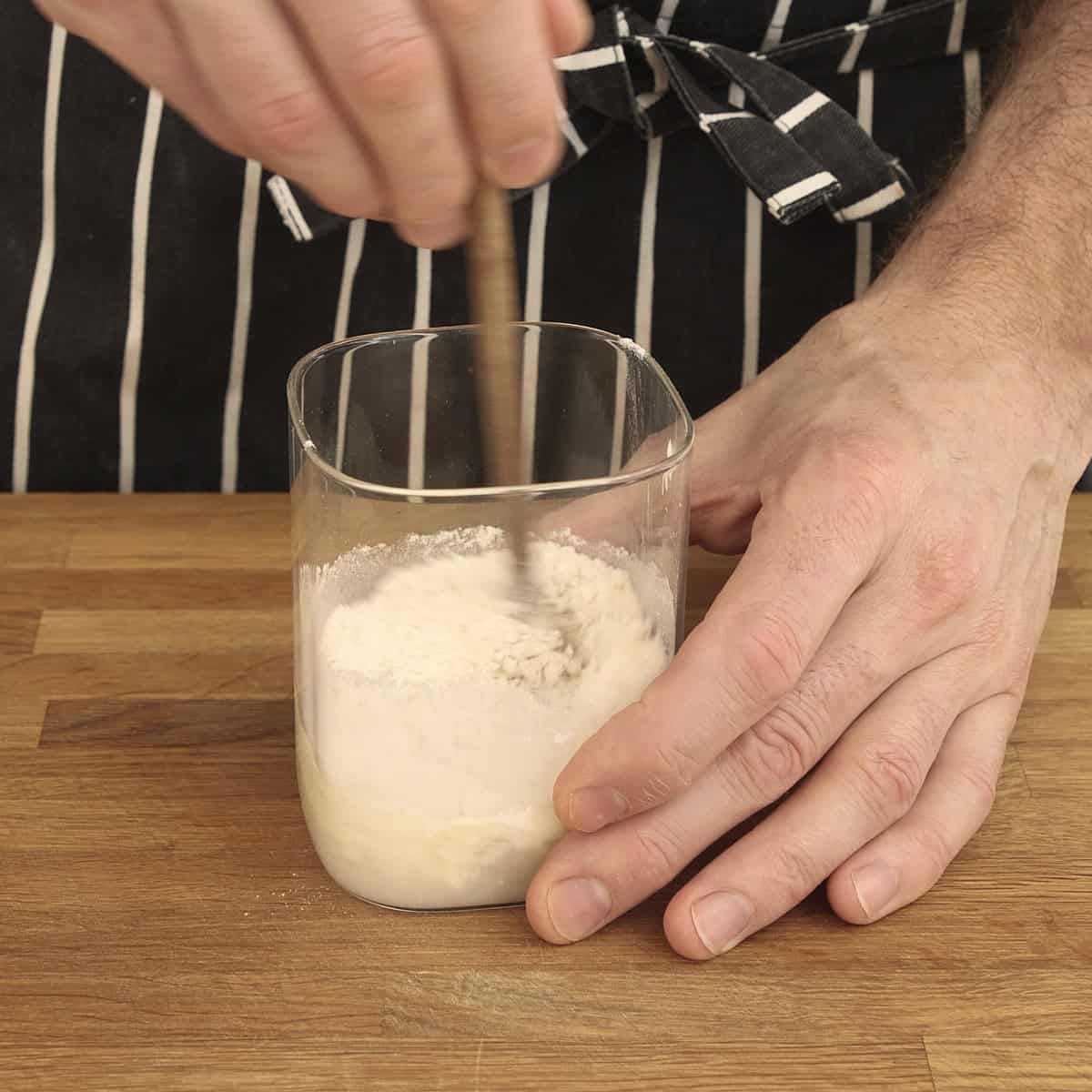 A hand mixes the sourdough starter with a wooden stick.