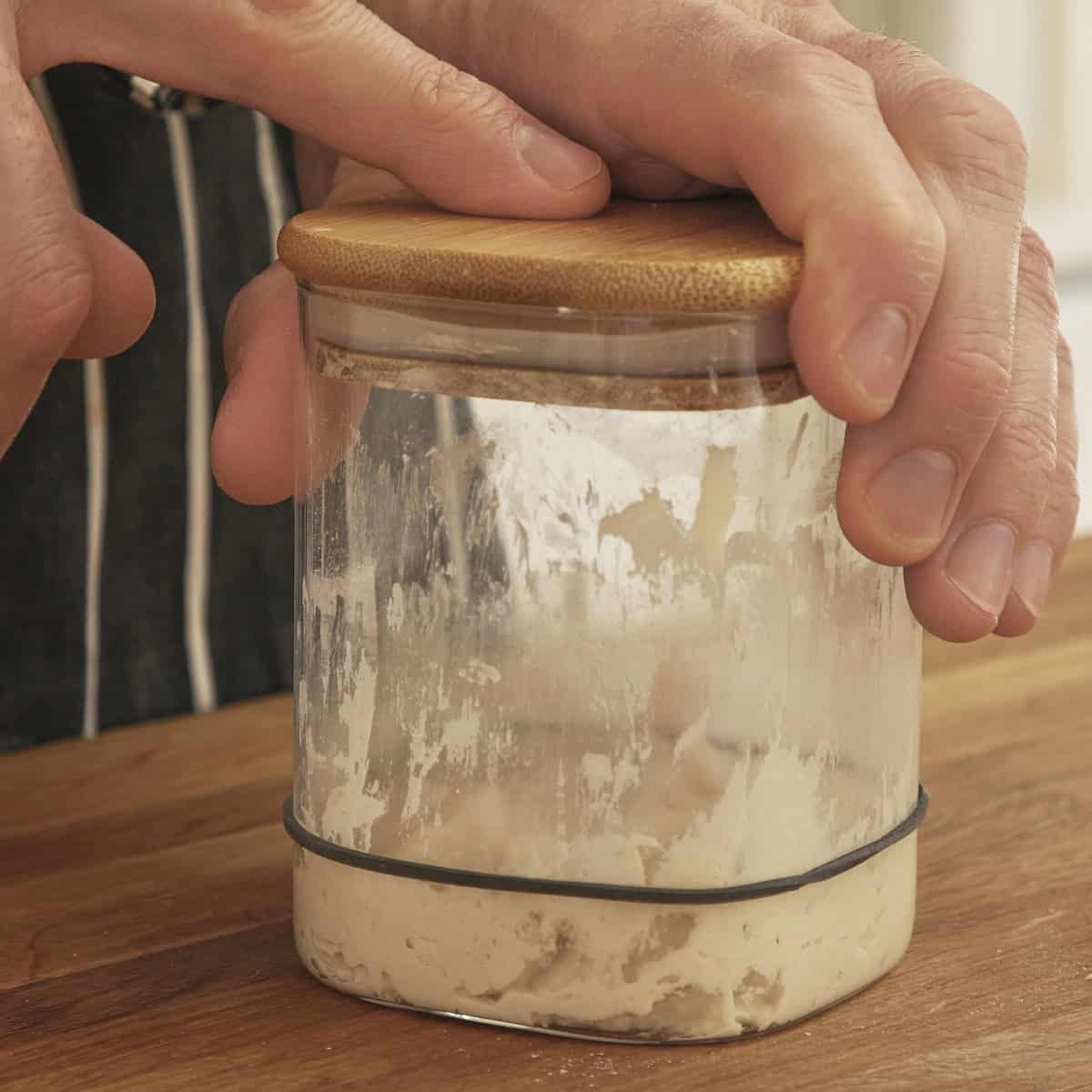 Mixed sourdough starter in a clear glass jar with a rubber band to track activity.