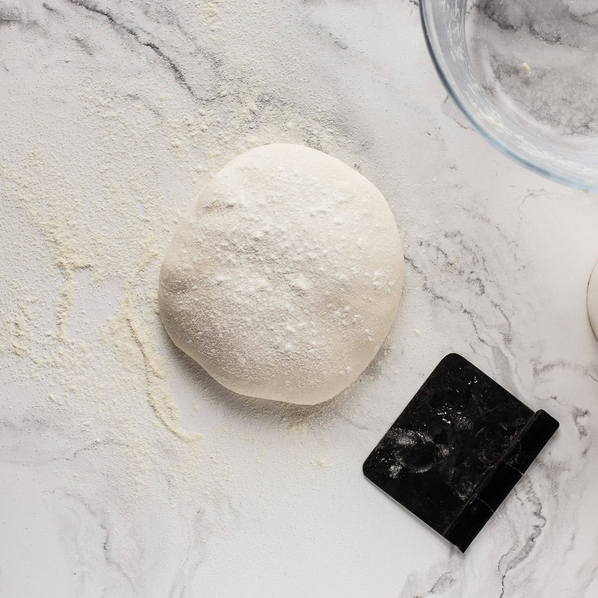 Dough and scraper on marble surface.