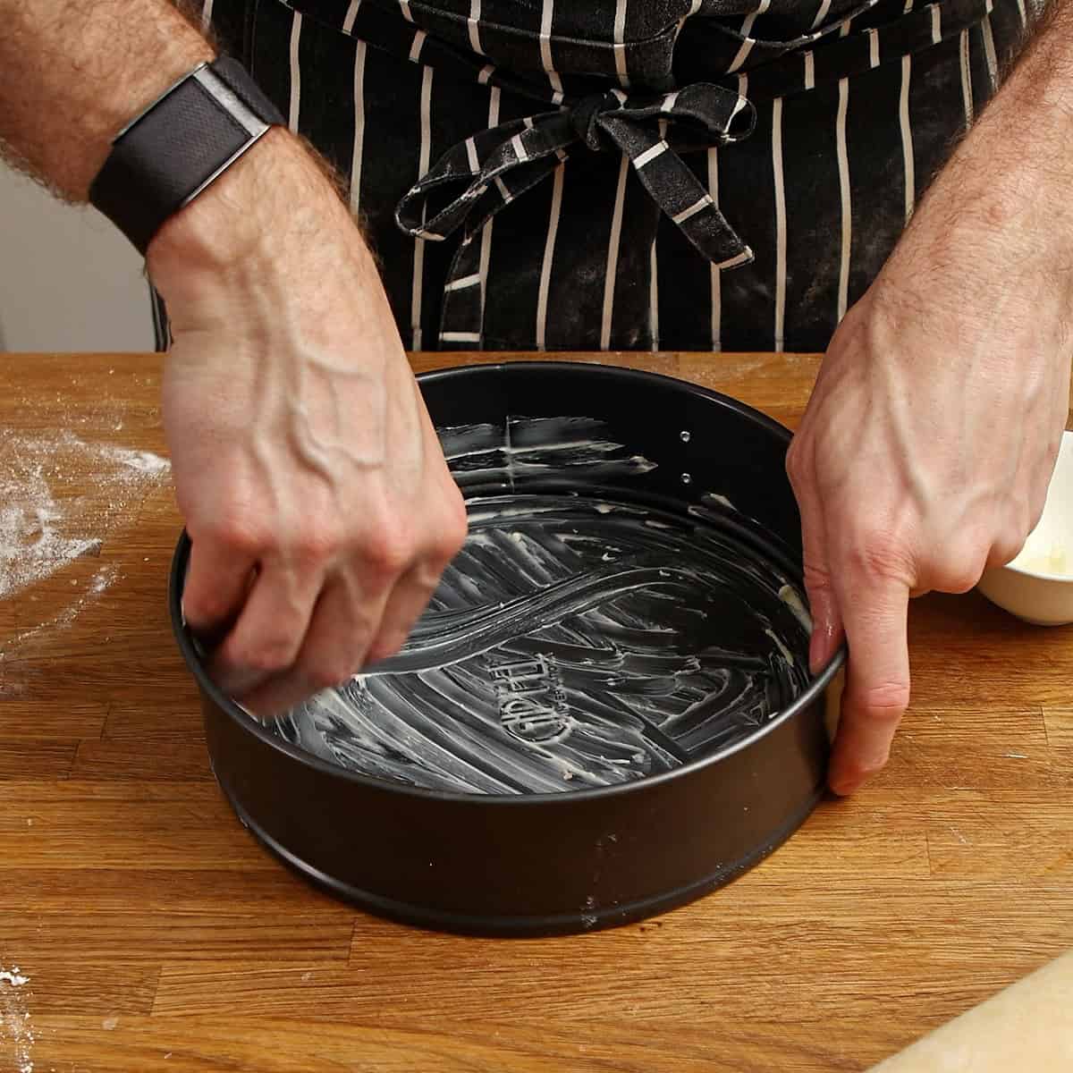 Hands buttering the inside of a round springform tin.