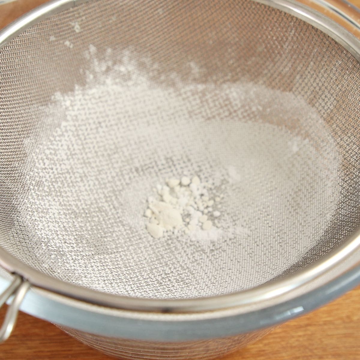 Cake flour, powdered sugar, and baking powder being sieved into a large mixing bowl