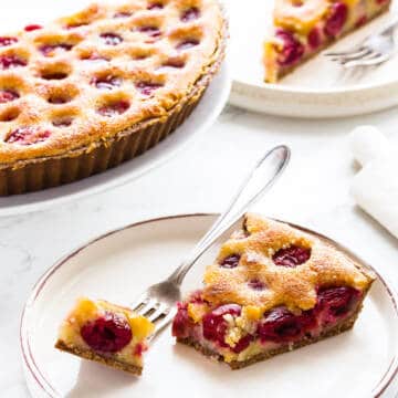 Cherry tart slice on white plate with fork.