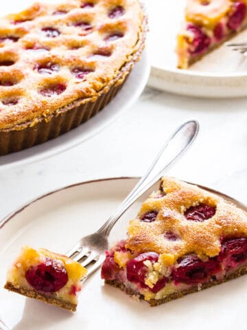 Cherry tart slice on white plate with fork.