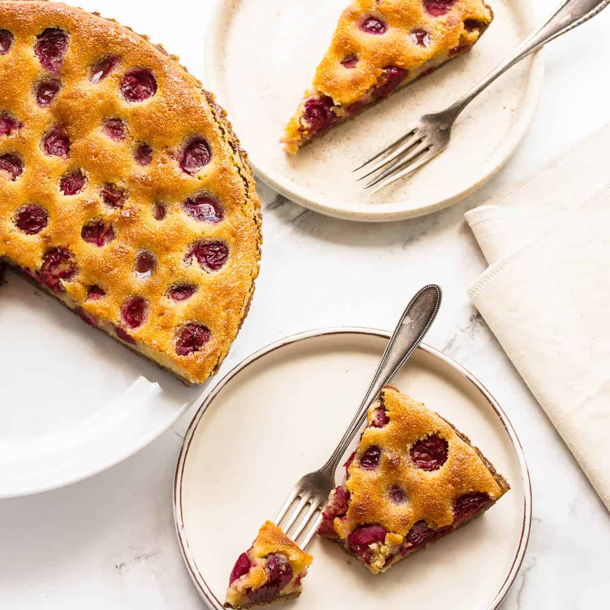 Cherry tart on white plates with forks on white background.